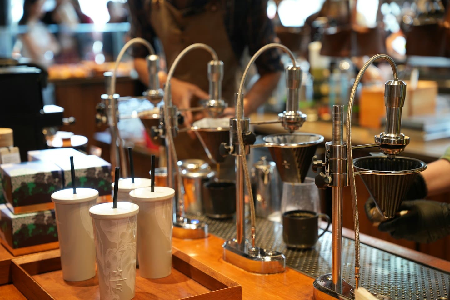 Barista uses professional chrome brewing equipment on a wooden counter.