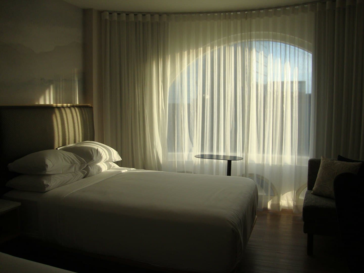 Minimalist hotel bedroom with a neatly made bed and arched window.