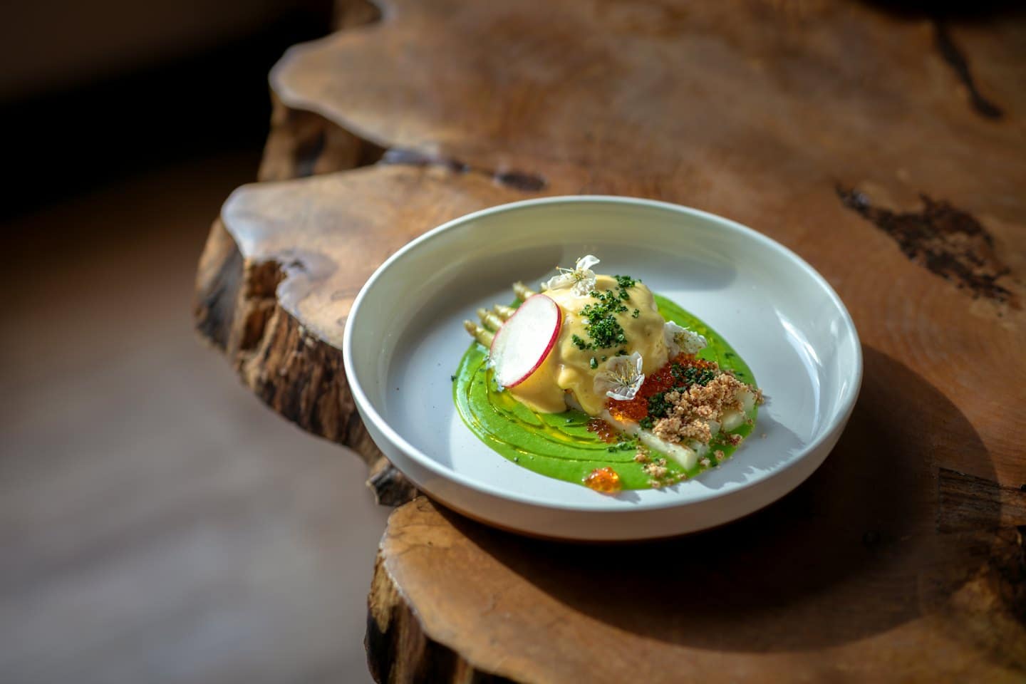 Gourmet dish with colorful sauce, roe, and flowers on wood table.