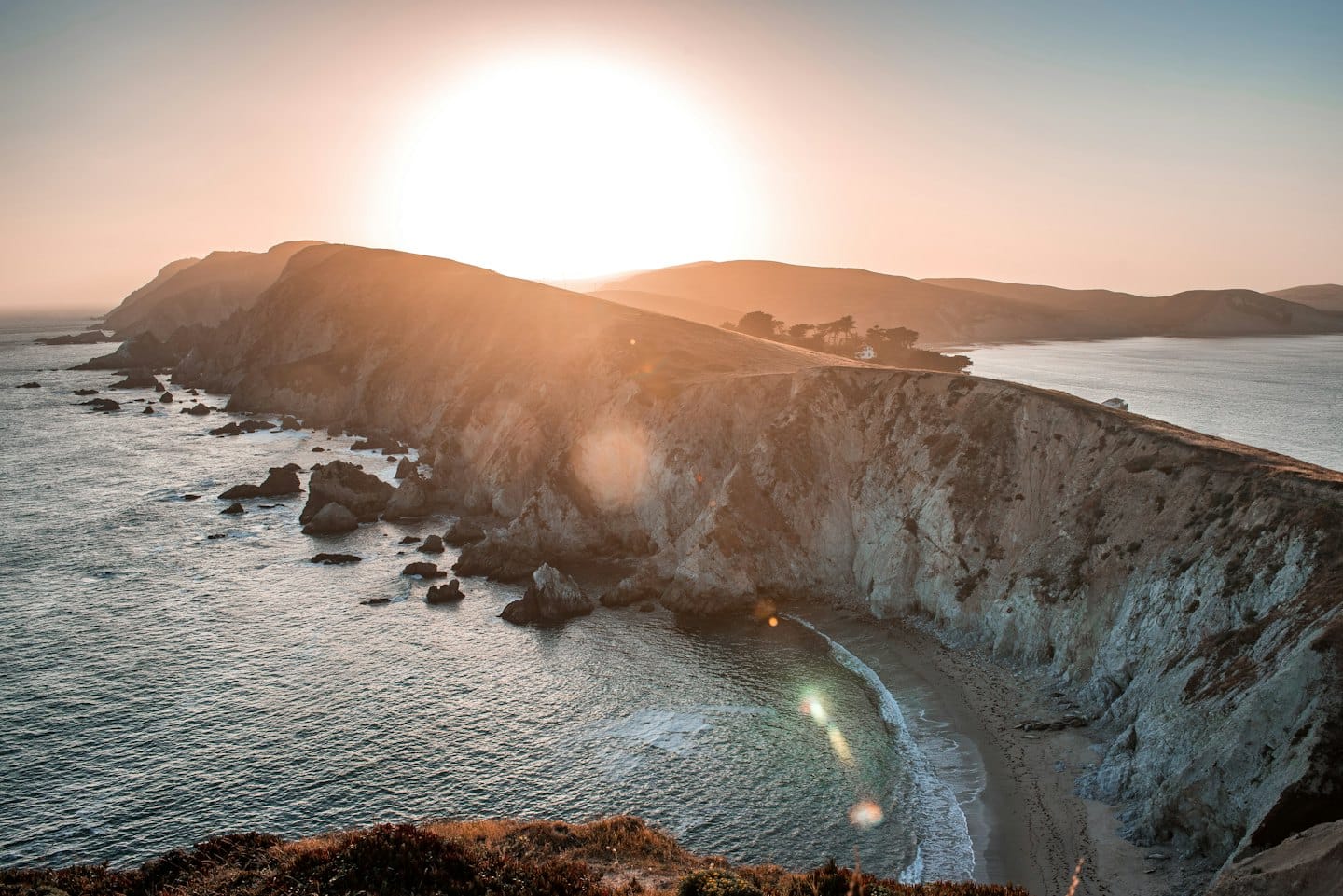 Rugged rocky coastline with a sandy beach at sunset.